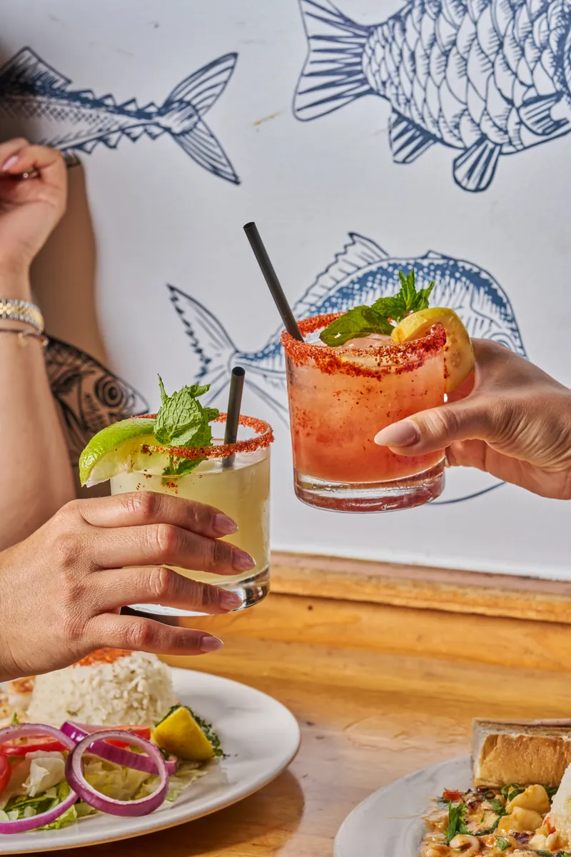 Two guests toasting cocktails over the fish mural